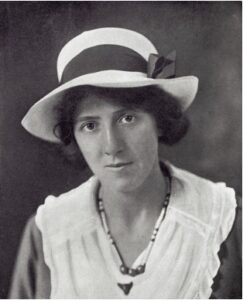 Black and white photograph of a young woman looking directly at the camera. She has a serious express and wears a white hat.