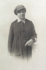 Black and white photograph of a young women wearing a hat and long dark coat.