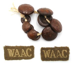Photograph of brown buttons with a cloth badge which is embroidered with WAAC